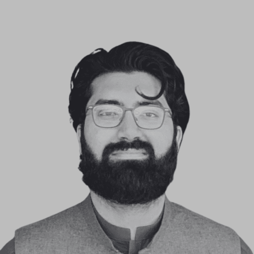 Black and white professional headshot of Hassan Shah, a SovDoc leadership team member, wearing glasses and a traditional vest against a neutral background.