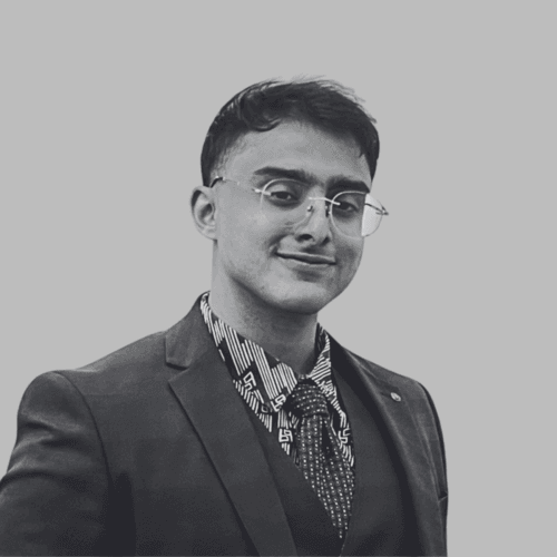 Black and white professional headshot of Adhil Razak, a SovDoc leadership team member, wearing glasses, a suit, and a patterned shirt against a neutral background.