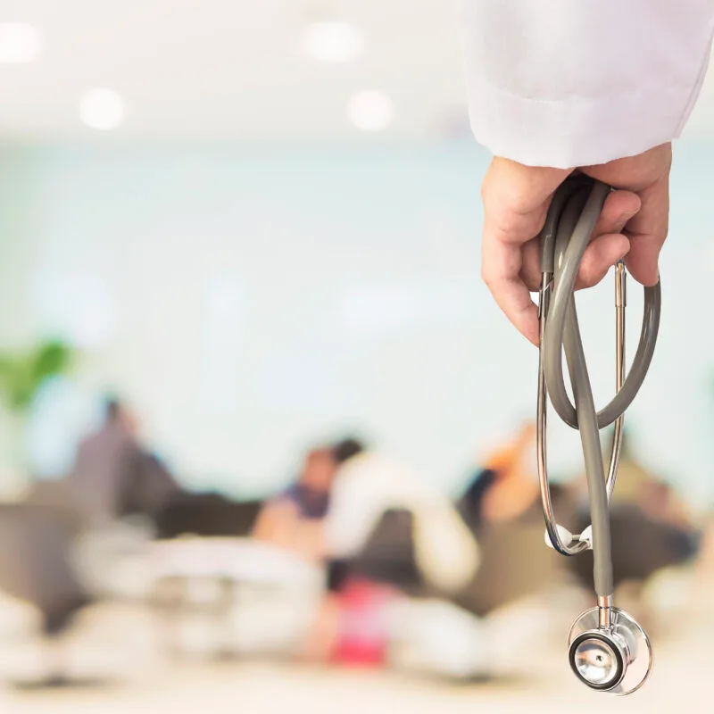 Doctor is going to examine his patient using his stethoscope over sitting people in modern hospital background